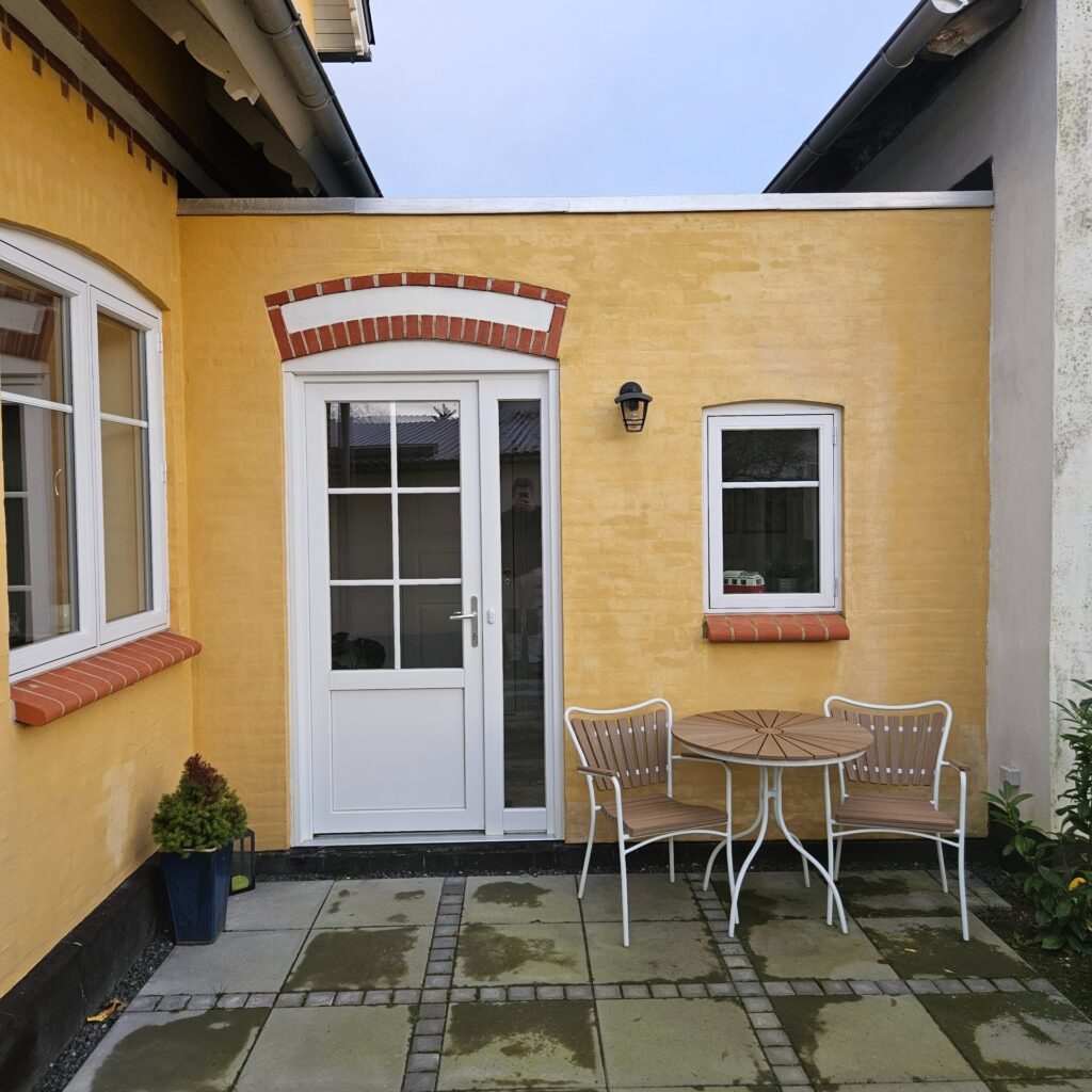 Ny dør og vindue i murstenshus – Hvid terrassedør og vindue i gul facade med røde detaljer.